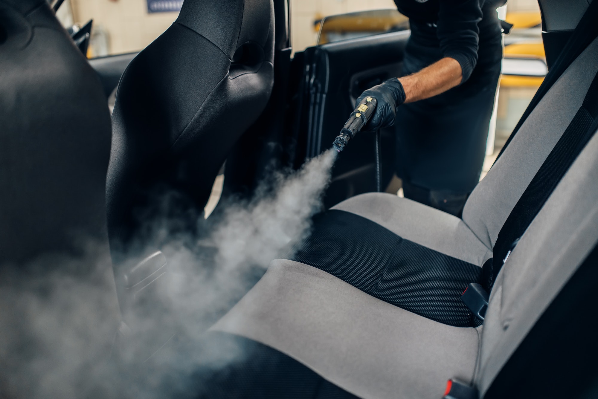 car wash worker cleans seats with steam cleaner